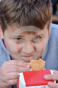 Full face portrait image of young cute boy eating fast food burger