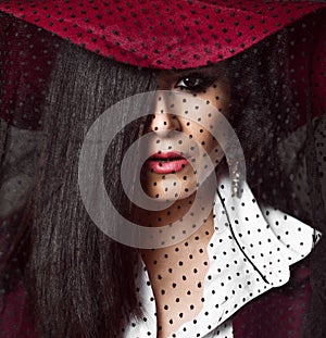 Full-face portrait of mysterious lady brunette in dark red hat with her veil down