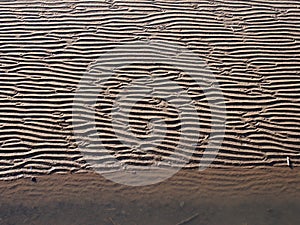 Full frame beach background with wavy pattered surface formed by water on the wet sand and shadow at the edge of the sea