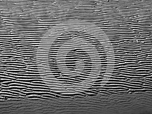 Full frame grey beach background with wavy pattered surface and water running in a line though the wet sand