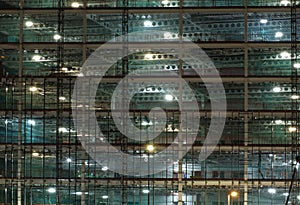 Full frame view of a large construction site at night illuminated by bright work lights with girders and construction hoists