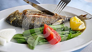 Man is eating frying fish with fork and knife in restaurant, dish closeup.