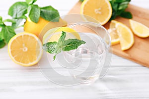 Full glass of fresh cool transparent water with lemon and mint leaves on wooden table