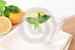 Full glass of fresh cool transparent water with lemon and mint leaves on wooden table. Close up