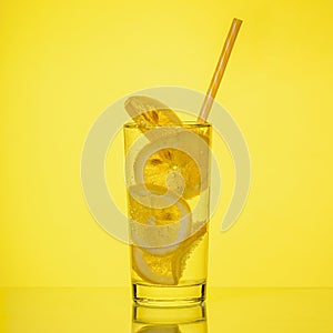 Full glass of fresh cool transparent water with lemon on yellow background
