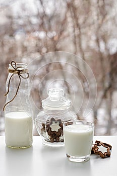 Full glass of milk, chocolate cookies and a bottle on breakfast table on window view