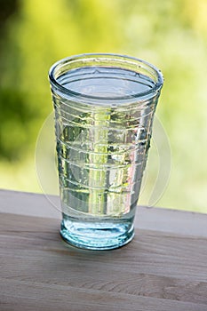 Full glass of water on the wooden kitchen counter. Green background.
