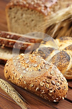 Full grain bread roll on wooden table with ear of rye