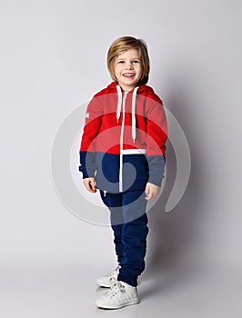 Full growth portrait of happy smiling blond kid boy in red and blue sportwear and white sneakers photo