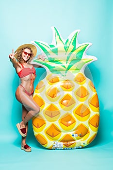 Full height of beautiful perfect body woman in sunglasses wearing in red bikini holding with pineapple mattress isolated on g