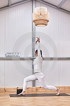 full image of attractive muscular young woman practicing hatha yoga at gym, standing barefooted on mat in Virabhadrasana 2 or