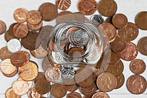 Full jar of coins from above, surrounded by loose change. Money saving and investment concept