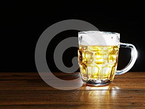 Full jar of lager beer with froth on a wooden table glowing in a dark. Alcohol consumption and sale. Copy space
