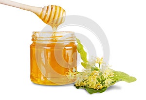 Full jar with linden honey, lime flowers and honey dripping from dipper into glass jar