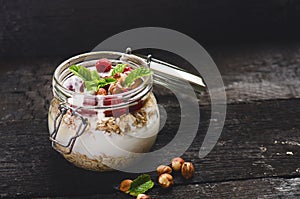 Full jar of muesli, yogurt, raspberries, nuts on a black, burnt wood table. Homemade breakfast cereals food. Healthy eating