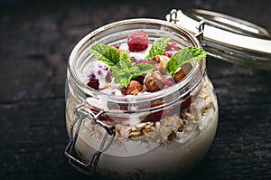 Full jar of muesli, yogurt, raspberries, nuts on a black, burnt wood table. Homemade breakfast cereals food. Healthy eating