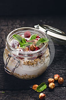 Full jar of muesli, yogurt, raspberries, nuts on a black, burnt wood table. Homemade breakfast cereals food. Healthy eating