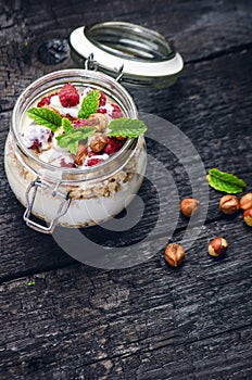 Full jar of muesli, yogurt, raspberries, nuts on a black, burnt wood table. Homemade breakfast cereals food. Healthy eating