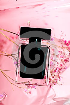 Full jar of perfume on pink background with water and flowers- Image