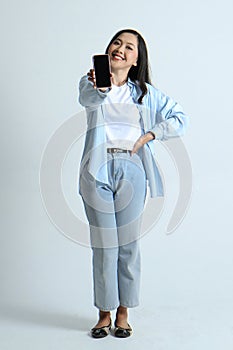 full leght shoot of happy asian indonesian woman holding phone and showing blank screen on isolated background