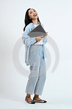 full leght shoot of happy asian Indonesian woman wearing casual attire, holding laptop on isolated background
