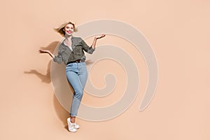 Full legth photo of funky excited woman dressed khaki shirt rising arms hands empty space isolated beige color