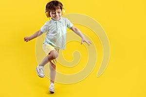 Full lengh photo of funny kid listening music in headphone and dance over yellow background.