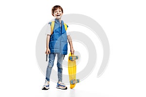 Full lengh photo of laughing little boy holding yellow skateboard on white background. Back to School.