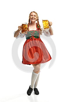 Full-lenght portrait of friendly young woman wearing folk German dirndl with two beer mugs over white background