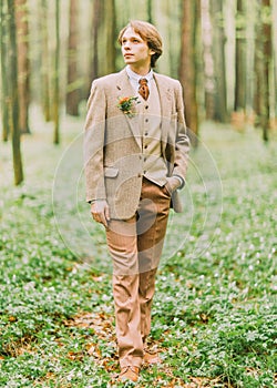 The full-lenght portrait of the man with blond hair in vintage suit looking at the sky and the mini-bouquet is pinned on