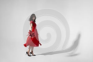 Full lengt image of a brunette young woman in red dress holding a bouquet of tulips and spins.