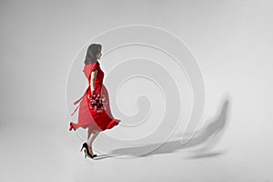 Full lengt image of a brunette young woman in red dress holding a bouquet of tulips and spins, isolated grey background.