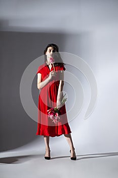 Full lengt image of a brunette young woman in red dress holding a bouquet of tulips and spins, isolated grey background.