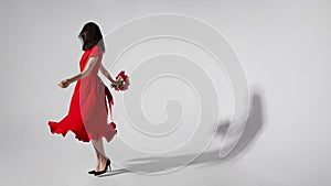 Full lengt image of a woman in red dress holding a bouquet of tulips and spins, isolated grey background.