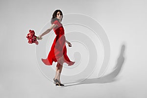 Full lengt view of a sensual young woman in dress holding a bouquet of tulips and spins, grey background. Copy space.