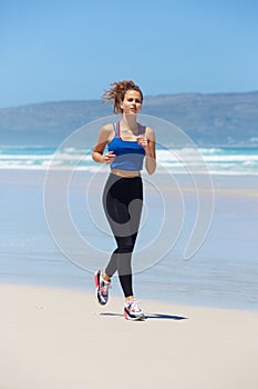 Full length active young woman running on beach