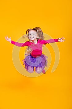 Full length adorable little girl in colorful clothes smiling and jumping on yellow background