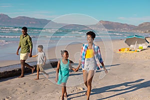 Full length of african american happy young parents with children walking at beach against sky