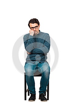 Full length of annoyed businessman keeps hand under cheek, seated on a chair isolated on white background. Business worker, wears