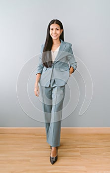 Full length of an attractive Asian businesswoman with toothy smile wearing wearing green suit and posing, looking at camera