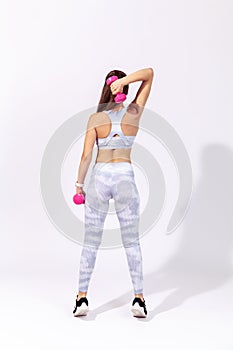 Full length back view athletic woman in white sportswear stretching her muscles and warming up doing fitness exercises with