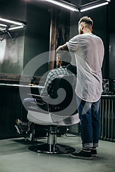 Full length of barber standing behind his client and cutting his hair