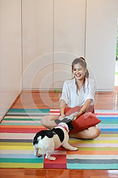 Full length beautiful young asian woman wearing white shirt and holding red pillow who sitting and playing with her cute dog with