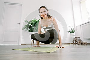 Full length of beautiful young sporty woman working out in yoga studio, doing arm balance exercise with crossed legs