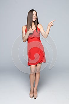 Full length of Beautiful young woman in red dress and high heels is standing, presenting at something and looking away isolated on