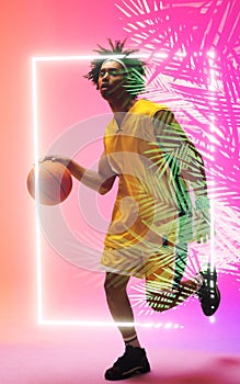 Full length of biracial basketball player dribbling ball by illuminated plants and rectangle