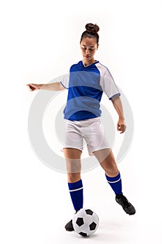 Full length of biracial young female soccer player kicking soccer ball against white background