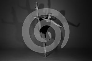 Full length black and white photo of beautiful young blonde ballet dancer in a black dress and pointes in complex pose