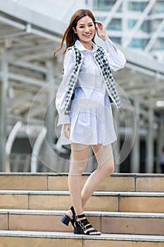 Full-length body portrait of cute smiling young adult Asian woman with a long brown haircut and fashionable white and black