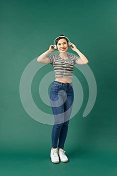 Full length body size photo of beautiful girl listening to music with headphones dancing singing song isolated on green background